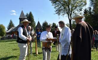 Ksiądz Proboszcz Grzegorz Kotarba odbiera bundz z rąk bacy Jana Bzdyk; Józef Michałek w guni, pasterz w czarnym brucliku, w tle kościół na Stecówce i ludzie