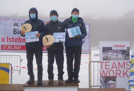 Panowie z kategorii M70 na podium – miejsce 1. Mazurek Kazimierz, miejsce 2. Faron Piotr, miejsce 3. Sikora Stefan z dyplomami i sttuetkami oraz voucherami w rękach; w tle baner imprezy