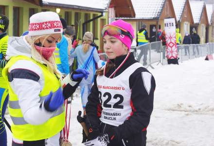 Amata Zuzanna na mecie wraz z Barbarą Juroszek w żółtej kamizelce organizatora; w drugim planie kilka przemieszczających się osób i zabudowania zaplecza organizacyjnego