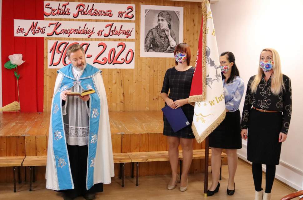 Proboszcz Parafii pw. Matki Bożej Fatimskiej na Stecówce ks. Grzegorz Kotarba czyta słowa modlitwy przedstawicielki Rady Rodziców ze sztandarem; w tle scena w bieli i czerwieni